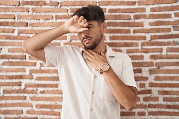 Wall Mural - Arab man with beard standing over bricks wall background touching forehead for illness and fever, flu and cold, virus sick