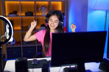 Canvas Print - Young chinese woman streamer playing video game with winner expression at gaming room