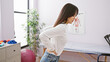© Krakenimages.com - Young asian woman experiencing backache at a modern clinic's rehab room, illustrating health and medical concepts.