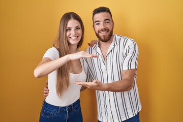 Wall Mural - Young couple standing over yellow background gesturing with hands showing big and large size sign, measure symbol. smiling looking at the camera. measuring concept.