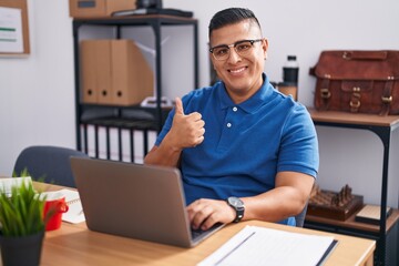 Sticker - Young hispanic man working at the office with laptop doing happy thumbs up gesture with hand. approving expression looking at the camera showing success.