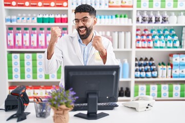 Sticker - Hispanic man with beard working at pharmacy drugstore very happy and excited doing winner gesture with arms raised, smiling and screaming for success. celebration concept.