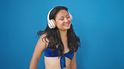 Canvas Print - Young chinese woman tourist wearing bikini listening to music dancing over isolated blue background