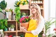 Young blonde woman florist smiling confident holding plant at florist