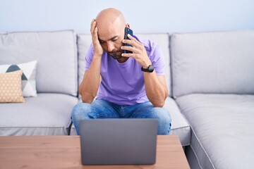 Canvas Print - Young bald man talking on smartphone with worried expression at home