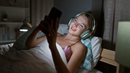 Wall Mural - Young blonde woman doing video call lying on the bed at bedroom