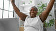 Confident african american woman, a successful business worker, raising arms in a celebrating gesture at her office desk, all smiles while working online on her laptop.