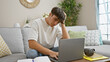 © Krakenimages.com - Stressed out young hispanic teenager sitting, studying on his laptop at home, face focused, struggling with online education on the living room sofa