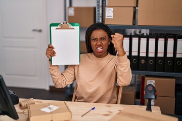 Poster - Young african american with braids working at small business ecommerce showing clipboard annoyed and frustrated shouting with anger, yelling crazy with anger and hand raised