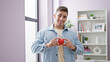 © Krakenimages.com - Beaming young hispanic man standing relaxed in living room, heart in hands, basking in comfort of home, enjoying life's simple joys