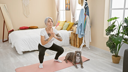 Poster - Middle-aged grey-haired woman trains her dog while exercising her legs in the bedroom, a lifestyle choice to stay fit and healthy