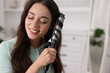 Smiling woman using curling hair iron at home. Space for text