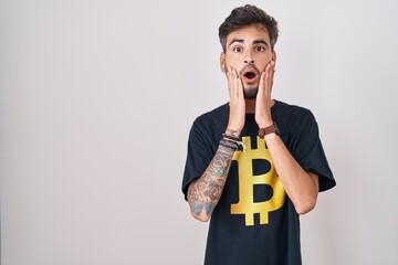 Poster - Young hispanic man with tattoos wearing bitcoin t shirt afraid and shocked, surprise and amazed expression with hands on face