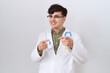 © Krakenimages.com - Young non binary man wearing doctor uniform and stethoscope pointing fingers to camera with happy and funny face. good energy and vibes.