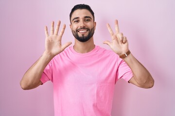 Sticker - Hispanic young man standing over pink background showing and pointing up with fingers number eight while smiling confident and happy.