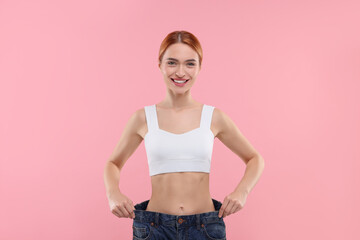 Poster - Slim woman wearing big jeans on pink background. Weight loss