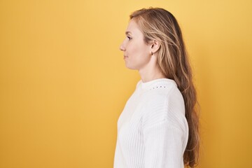 Poster - Young caucasian woman wearing white sweater over yellow background looking to side, relax profile pose with natural face and confident smile.