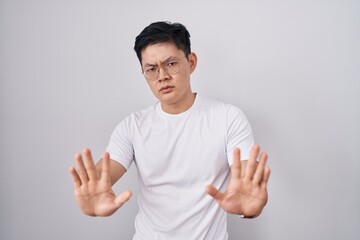 Sticker - Young asian man standing over white background moving away hands palms showing refusal and denial with afraid and disgusting expression. stop and forbidden.