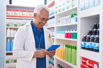 Wall Mural - Middle age grey-haired man pharmacist using touchpad working at pharmacy