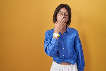 Wall Mural - Young girl standing over yellow background bored yawning tired covering mouth with hand. restless and sleepiness.