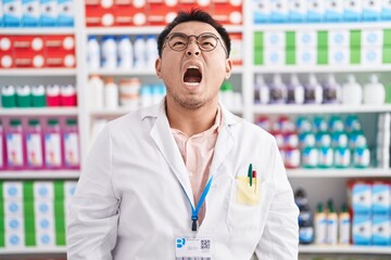 Sticker - Chinese young man working at pharmacy drugstore angry and mad screaming frustrated and furious, shouting with anger. rage and aggressive concept.