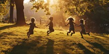 Four Children Joyfully Leap And Bound Across The Grassy Park Field, Basking In The Enchanting Play Of Beautiful Light And Shadows.