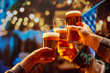 Close up image of hands holding glasses of beer and clinking after celebrating toast. Old friends sitting in bar and celebrating start of football season. Concept of Oktoberfest, party, traditions.