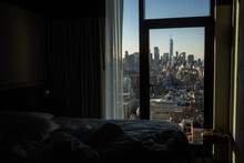 A View Of The Manhattan Skyline From A Midtown New York City Hotel Bedroom, Including Views Of One World Trade Center.  Sunny Day With Blue Skies, And An Unmade Bed In The Foreground.