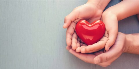 Wall Mural - Hands of mother and daughter holding a red heart on a wooden background