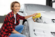 Blonde woman in checkered shirt washing a white car