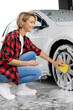 Blonde woman in checkered shirt washing a white car
