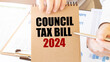 Text COUNCIL TAX BILL 2024 on brown paper notepad in businessman hands on the table with diagram. Business concept