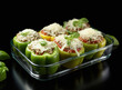 stuffed peppers with grated cheese and basil leaves on a black background, cooking in a glass baking dish