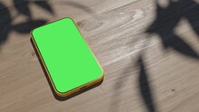 A phone lying on a table, an animation of a gadget on a wooden table. the video has a green screen with shadows from the foliage