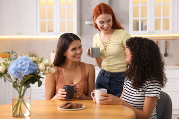 Wall Mural - Happy young friends with cups of drink spending time together in kitchen