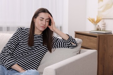 Canvas Print - Sad woman suffering from headache on sofa indoors