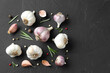 Fresh garlic, rosemary and peppercorns on dark textured table, flat lay. Space for text