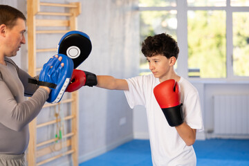 Adult man and boy teenager train boxing punches in studio