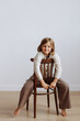 © Kaplitskaya Love - A Caucasian child sits on a classic wooden chair against a minimalist grey backdrop. Concept for family-oriented advertisements or child development content.