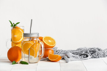 Mason jar and glass of infused water with orange slices on white tile table