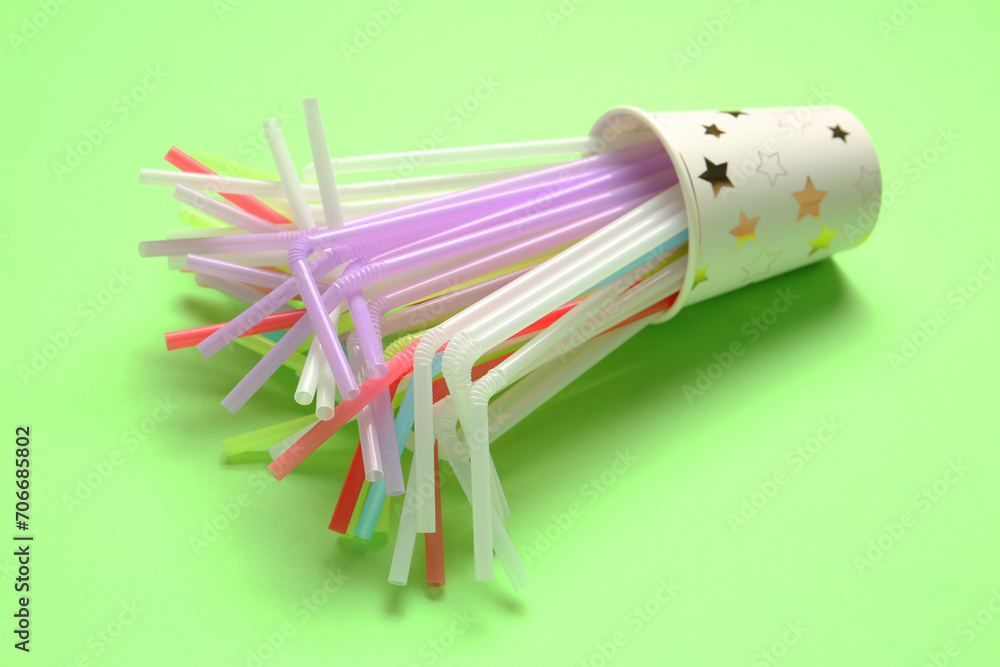 Paper cup with different colorful straws on green background