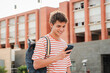 © Jose Calsina - Male student having fun with a cellphone posting on the social media at university campus. Real teenage guy smiling using a smartphone. Young man holding a mobile phone. Teen schoolboy reading a phone