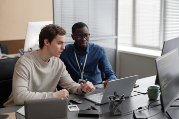 caucasian male junior it specialist sitting at table and explaining new cybersecurity software code 