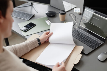 over the shoulder shot of unrecognizable it worker holding blank papers in cardboard folder while si