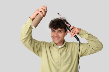 Sticker - Handsome young man using hair spray and curling iron on grey background