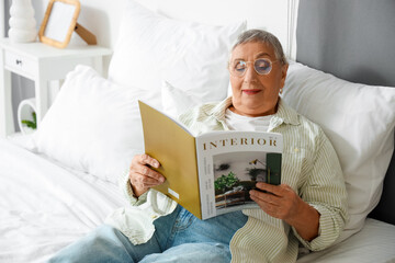 Senior woman with eyeglasses reading magazine in bedroom