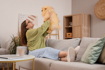 Young woman with cute Pomeranian dog resting on sofa at home