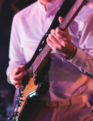 Concert view of an electric guitar player with vocalist and rock band performing in a club, male musician guitarist on stage with audience in a crowded concert hall arena