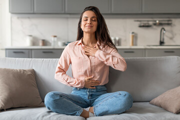 Wall Mural - Relaxed young woman meditating on sofa at home