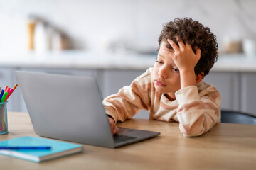 Upset black schoolboy tired of doing homework on laptop